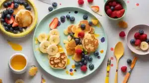 A vibrant breakfast idea for toddlers featuring mini pancakes, veggie-packed scrambled eggs, and colorful rainbow fruit skewers.