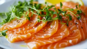 Salmon crudo with thin, rich orange slices, drizzled with olive oil and garnished with microgreens, citrus zest, and flaky sea salt on a white ceramic plate. A fresh, glistening dish against a blurred fine dining backdrop.