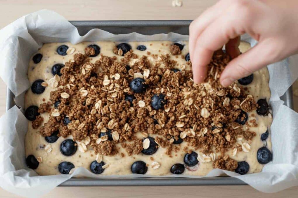 Sprinkling crumb topping on Blueberry Muffin Bread batter in loaf pan