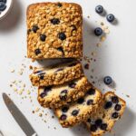 Sliced Blueberry Muffin Bread loaf with crunchy oat streusel and whole blueberries on a light surface.