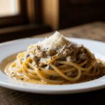 Plate of spaghetti carbonara coated in creamy egg sauce, topped with grated Pecorino cheese and cracked black pepper on a rustic wooden table