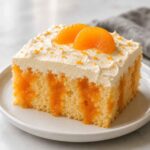 Orange Creamsicle Poke Cake – Moist, Easy, and Worth the Wait 9 Orange creamsicle poke cake slice with orange gelatin ribbons, vanilla mousse topping and mandarin orange segments on white plate